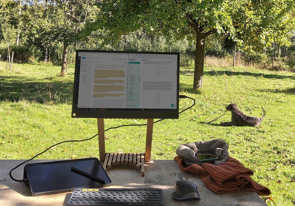 Garden view with in the forefront a desk with  a tablet, keyboard, mouse and Foote.