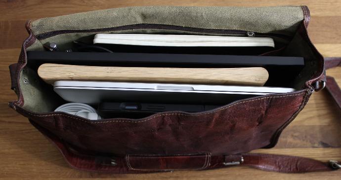 Top view of a leather bag containing laptop, Foote, tablet ,charger and a notebook.